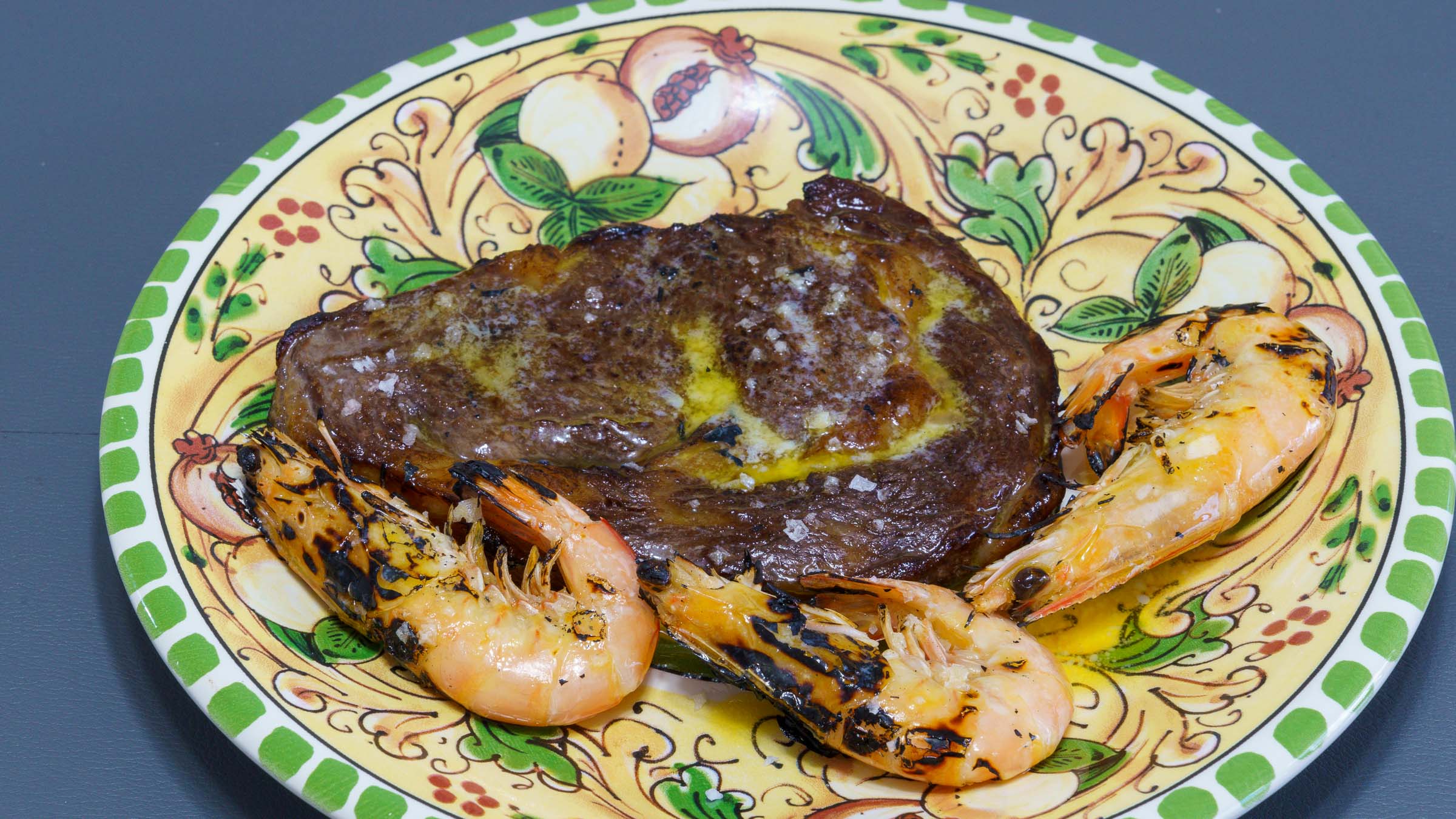 A floral dinner plate featuring pomegranates with a perfectly cooked scotch fillet steak and three freshly flame torched South Australian king prawns