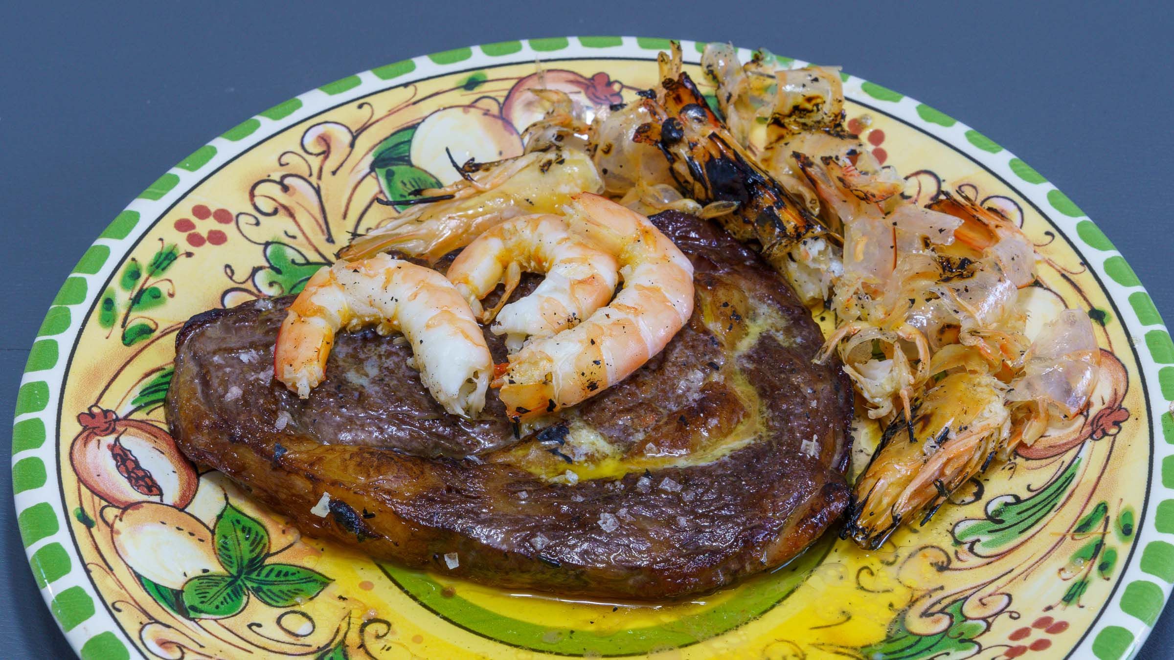 A floral dinner plate featuring pomegranates with a perfectly cooked scotch fillet steak and three freshly flame torched South Australian king prawns