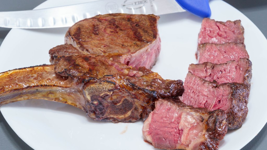 A photograph of a bone-in ribeye steak with the bone, fillet, and sliced deckle (spinalis) meat dissected apart.