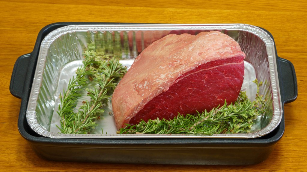 A photograph of the uncooked beef in a roasting tray with sprigs of rosemary.