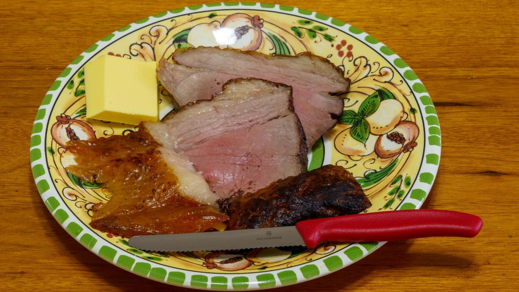 A photograph of the cooked beef sliced on a dinner plate. It has a bit of butter to one side plus a new red handled Victorinox steak knife.