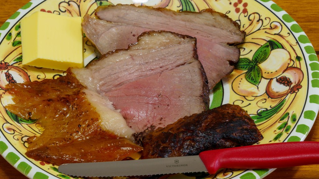 A photograph of the cooked beef sliced on a dinner plate. It has a bit of butter to one side plus a new red handled Victorinox steak knife.