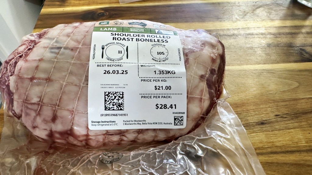 A photograph of a lamb shoulder rolled boneless roast in it's plastic packaging on a cutting board. The piece of meat weighed 1.35 kg and cost $21/kg. The total price was $28.41.