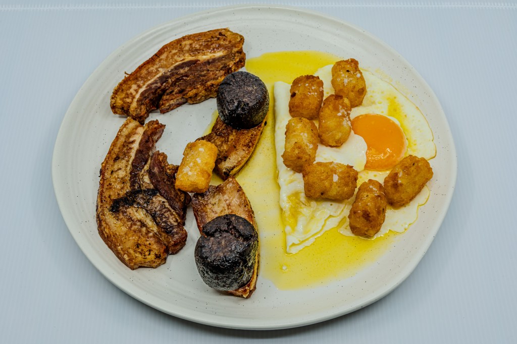 Photograph of a plate of barbecued pork rashers and black pudding, eggs fried in butter, and potato gems fried in beef fat.
