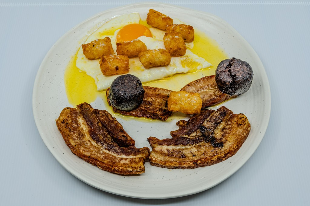 Photograph of a plate of barbecued pork rashers and black pudding, eggs fried in butter, and potato gems fried in beef fat.