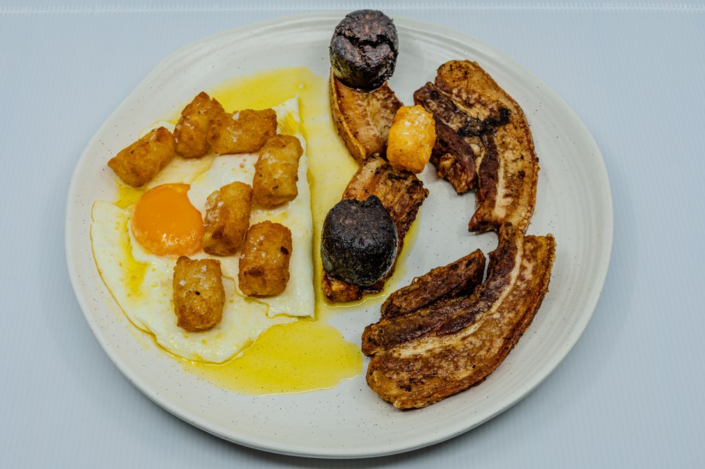 Photograph of a plate of barbecued pork rashers and black pudding, eggs fried in butter, and potato gems fried in beef fat.