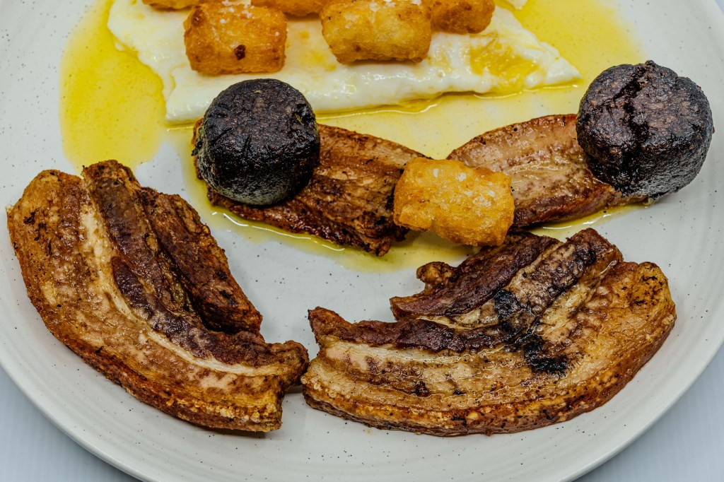 Photograph of a plate of barbecued pork rashers and black pudding, eggs fried in butter, and potato gems fried in beef fat.