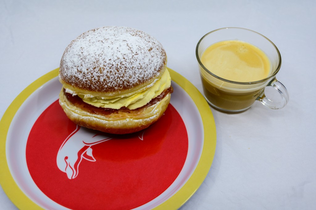 Cream bun and coffee. The plate for the cream bun is a piece of Dolphins NRL merchandise.