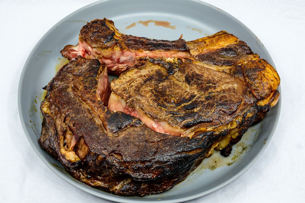 Photograph of Bone-in ribeye steak after being seared on a hot cast-iron flat top barbecue grill with a gas torch. Dissected from the rib bone and the spinalis separated from the longissimus dorsi muscle.