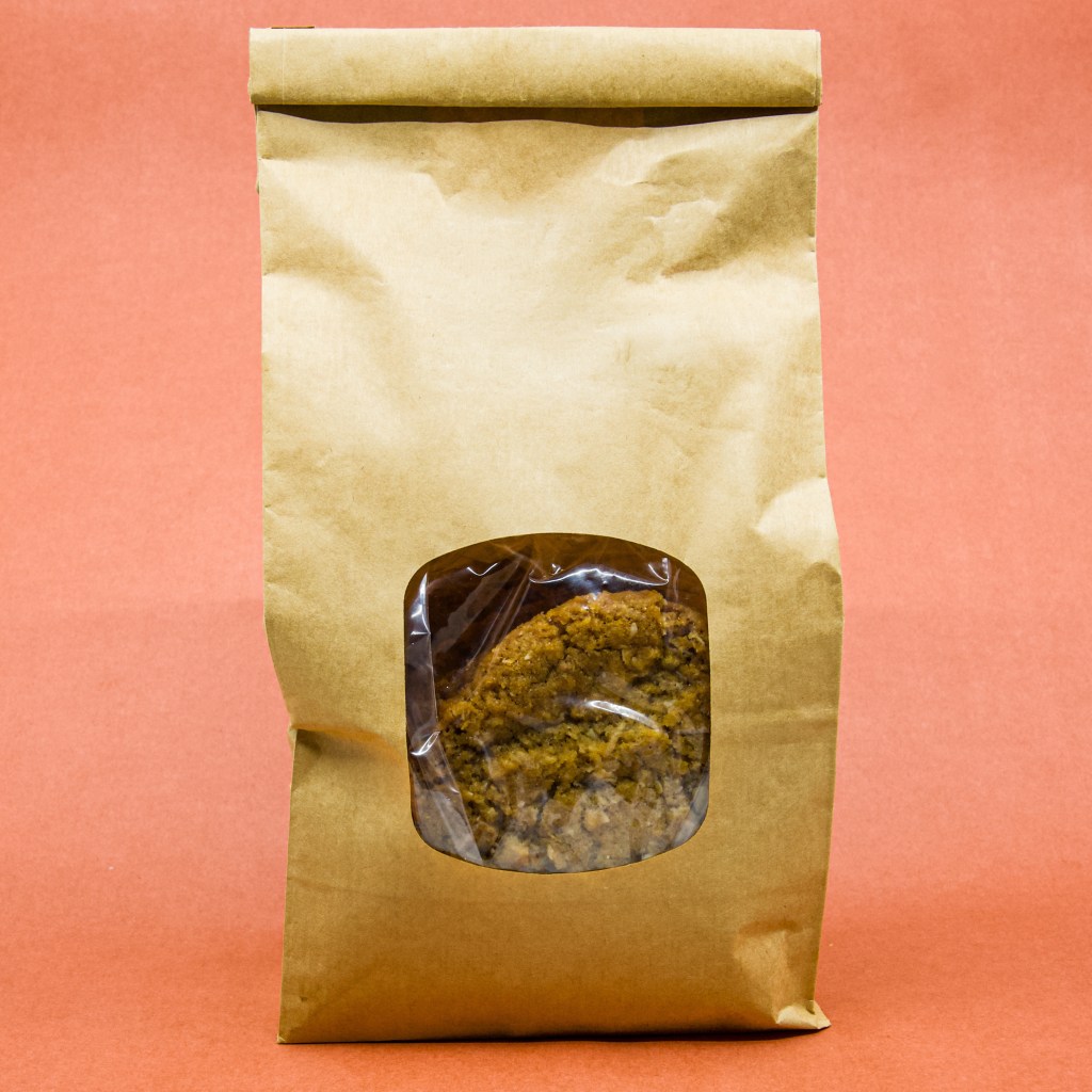 Brown paper bag with a clear window containing Anzac biscuits.