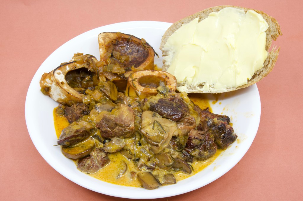 A photograph of a bowl with a rich creamy sauce with beef shank, mushrooms and bone marrow is served with rye sourdough and cultured butter.