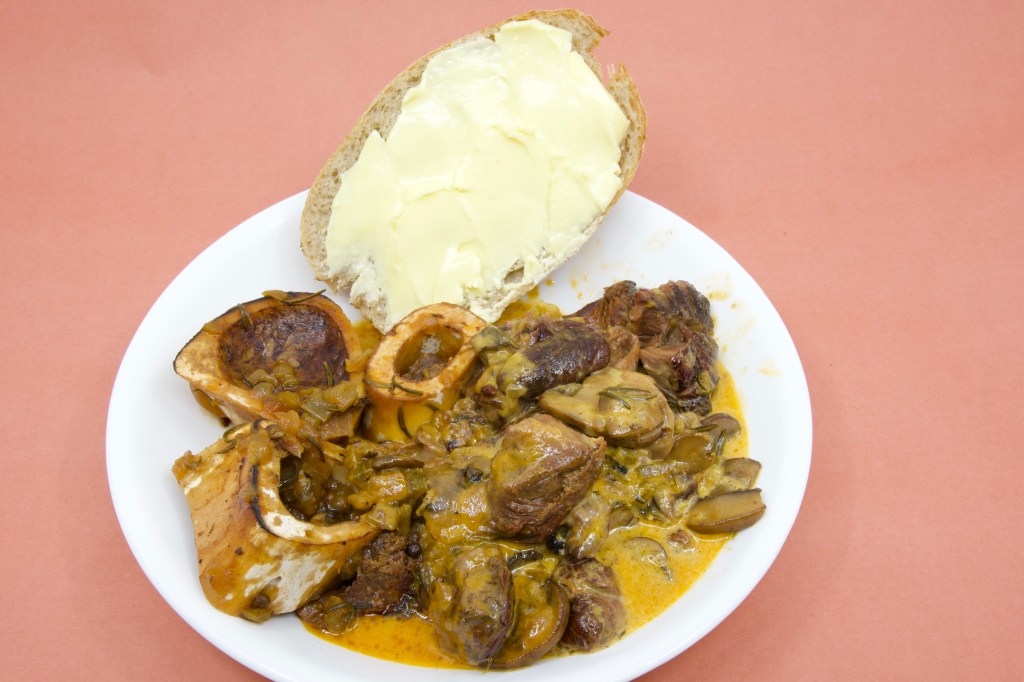 A photograph of a bowl with a rich creamy sauce with beef shank, mushrooms and bone marrow is served with rye sourdough and cultured butter.