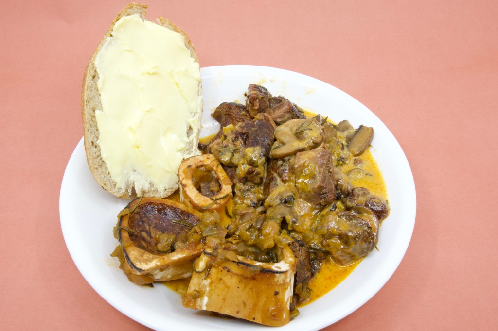 A photograph of a bowl with a rich creamy sauce with beef shank, mushrooms and bone marrow is served with rye sourdough and cultured butter.