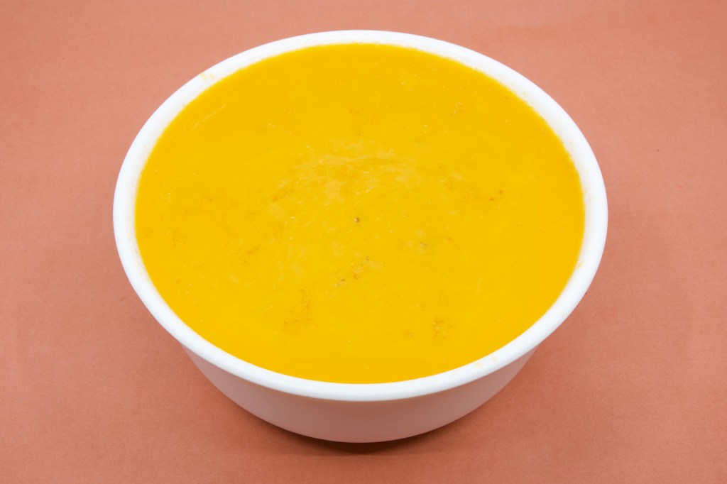 A photograph of a bowl with chilled pork rib cooking liquor. The surface of the fluid is solid with pork and beef fat. The fat is orange in colour. The bowl is white in colour.