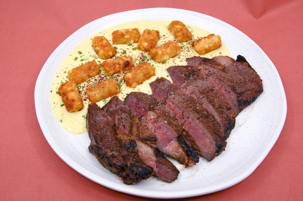 Torch-seared scotch fillet steak sliced and arranged beside crisp potato gems cooked in beef fat. The meal is presented on a creamy blue cheese and Dijon mustard sauce, finished with cracked pepper and green chive garnish.