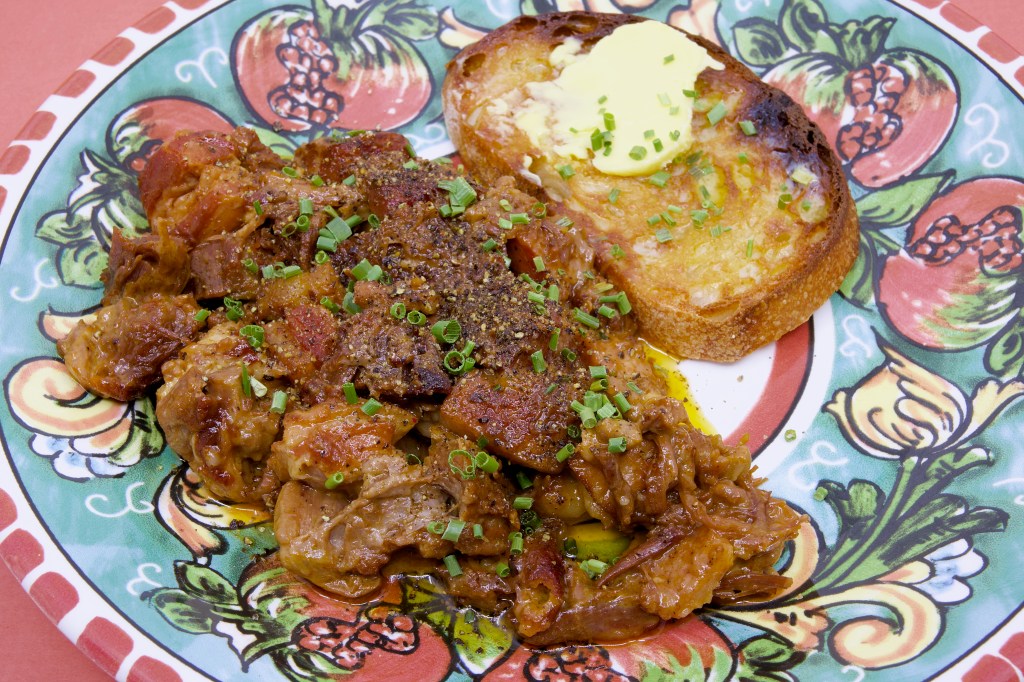 Close-up of pressure-cooked beef, lamb, and pork stew garnished with cracked black pepper and chopped chives, served with double-buttered rye sourdough toast.