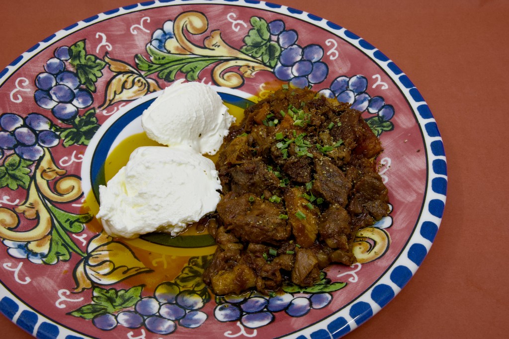 Mixed mammal stew containing beef, lamb, and pork served on a decorative plate with two scoops of Greek-style yoghurt and a garnish of chopped chives.