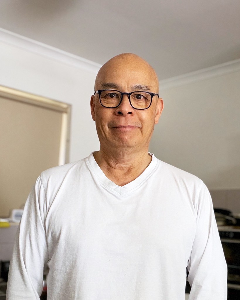 Food blogger standing in a home kitchen wearing glasses and a white long-sleeved shirt before preparing an Instant Pot pork and pancetta recipe.