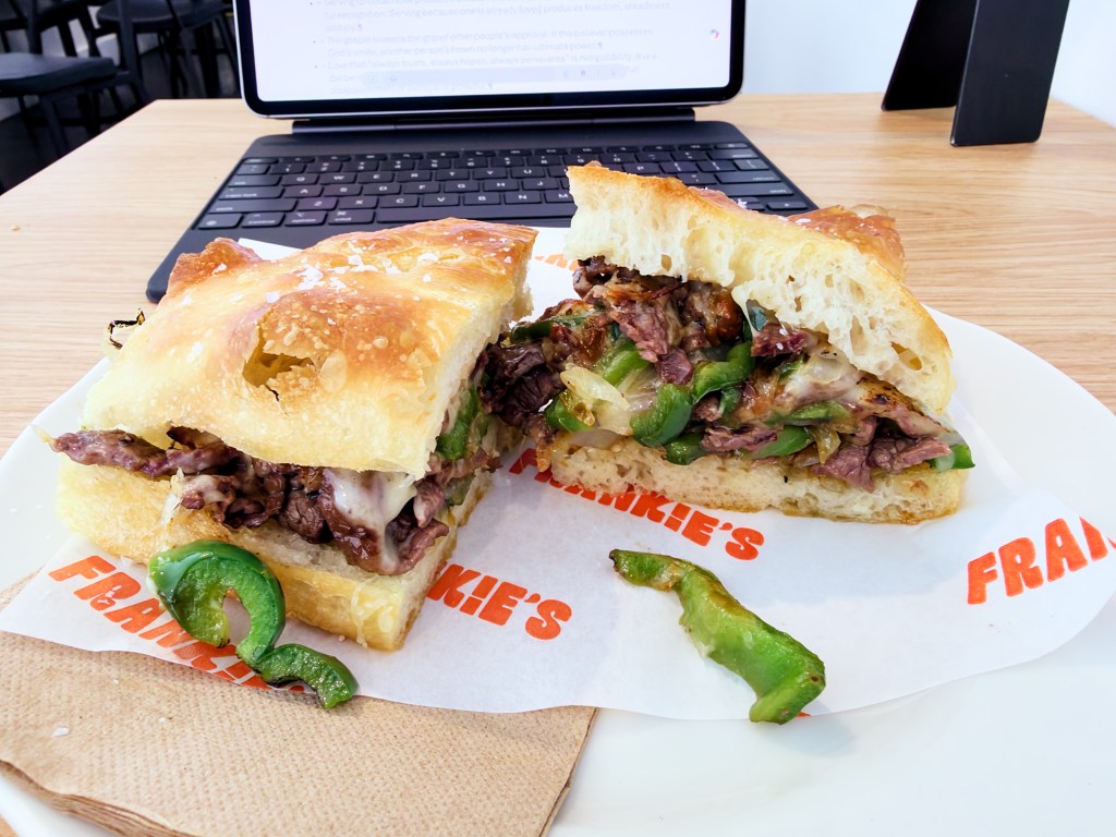 Close view of a cheesesteak focaccia sandwich on Frankie’s branded paper, filled with tender beef, melted cheese, green capsicum, and onion.